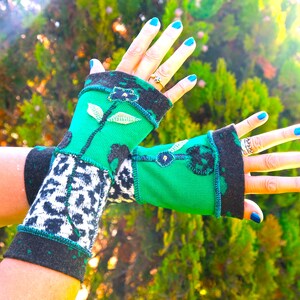 Pode incluir: Um par de luvas sem dedos com uma base verde vibrante e bordados florais e de folhas pretas. As secções inferiores apresentam um padrão de leopardo a preto e branco, com punhos cinzento-escuro e costuras visíveis em azul-petróleo.