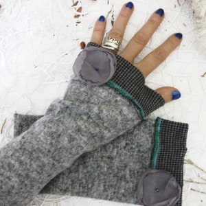 May include: Gray fingerless gloves with a black and white checkered pattern and a gray flower embellishment on each cuff. The gloves have a green and blue trim.