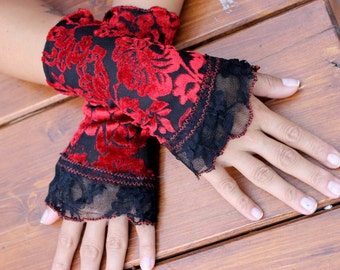 May include: A pair of red velvet and black lace fingerless gloves. The gloves have a floral pattern and are trimmed with black lace.