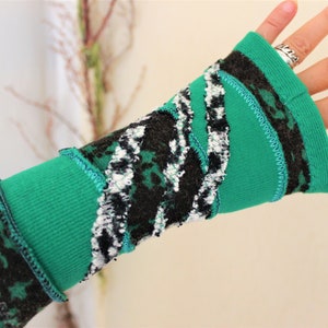 Könnte beinhalten: Ein fingerloser Handschuh mit einem Patchwork-Design aus einfarbigem, hellgrünem Stoff und schwarz-weiß strukturiertem Stoff. Die Abschnitte sind mit sichtbaren türkisfarbenen Zickzacknähten verbunden, was einen geschichteten Look über Handgelenk und Handfläche erzeugt.