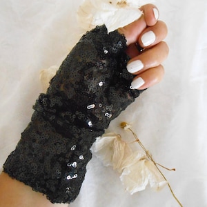 May include: Black sequined fingerless gloves with a sheer fabric base. The gloves are gathered at the wrist and have a loose fit.