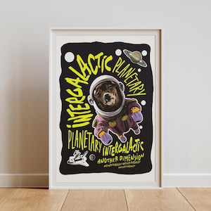 May include: A framed art print featuring a bear in an astronaut suit against a black background. The words "Intergalactic Planetary" are in yellow, stylized text. A Saturn-like planet and a spaceship are also depicted.