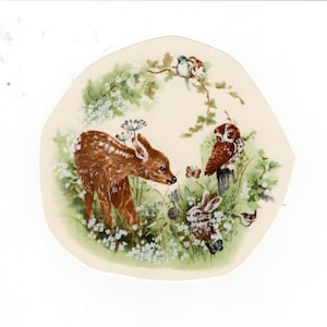 May include: A charming illustration featuring a fawn, rabbit, and owl in a woodland scene. The artwork, set against a cream backdrop, includes white flowers, green foliage, butterflies, and birds. The overall design evokes a sense of nature.