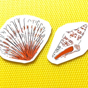Puede incluir: Dos pegatinas de papel troqueladas con ilustraciones detalladas de conchas marinas. Una muestra una concha de abanico con líneas de tinta naranja y negra, mientras que la otra representa una concha espiral con detalles de tinta similares.