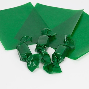 May include: Four green candy wrappers with a green square sheet of wrapping paper in the background.