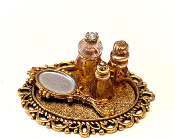 Bandeja de tocador en miniatura para casa de muñecas con espejo de mano y frascos de perfume ámbar.