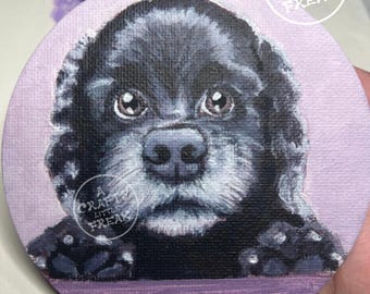 May include: A round, hand-painted coaster featuring a black Cocker Spaniel puppy with big, expressive eyes. The background is a soft lavender, and the coaster has the text "A Crafty Little Freak" in a white circle.