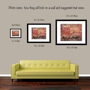 May include: Three framed photos of different sizes showing a brick wall with the text "tout est possible" written in black paint. The photos are hanging on a light brown wall above a yellow couch.