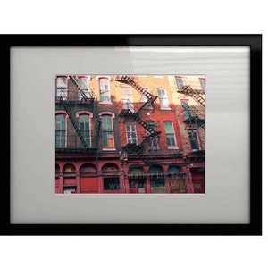 May include: A photograph of a row of brick buildings with fire escapes. The buildings are painted in shades of red, orange, and yellow. The fire escapes are made of metal and are painted black.