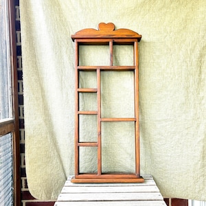 May include: A tall, rectangular wooden wall shelf featuring a medium brown finish and a decorative heart-shaped cutout at the top center. The unit is divided into multiple open compartments of varying sizes, arranged in an asymmetrical grid pattern.