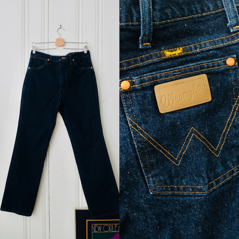 Peut inclure: Un jean Wrangler en denim bleu fonc&eacute;, suspendu &agrave; un cintre en bois. Le jean a une taille haute et une coupe droite. La poche arri&egrave;re pr&eacute;sente le logo et les coutures Wrangler. Un style classique.