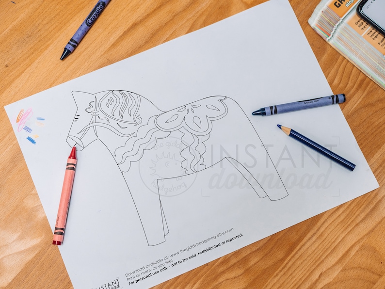 May include: A black and white line drawing of a Dala horse, a traditional Swedish wooden toy horse, on a white sheet of paper. Crayons and pencils are visible on the table.