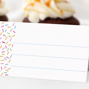 May include: White place card with a colorful sprinkle pattern on the left side. The card has four blue lines across the white surface.