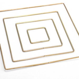 May include: Four gold-colored metal hoops, each a square shape, are nested inside each other, creating a concentric pattern. The hoops are arranged in decreasing size, with the largest hoop at the bottom and the smallest hoop at the top.