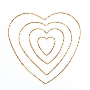 May include: Four gold metal heart-shaped hoops, nested inside each other, on a white background.