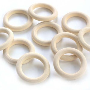 May include: Ten natural wood rings, each with a smooth, unfinished surface. The rings are all the same size and shape, and they are arranged in a random pattern.
