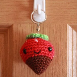 May include: A crocheted strawberry keychain with a chocolate-dipped bottom, green leaves, and a smiling face.