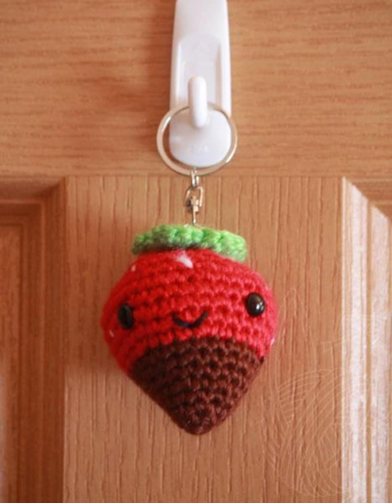 May include: A crocheted strawberry keychain with a chocolate-dipped bottom, green leaves, and a smiling face.
