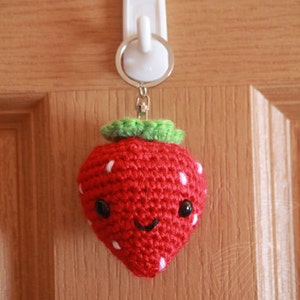 May include: A crocheted strawberry keychain with a smiling face, white dots, and green leaves.