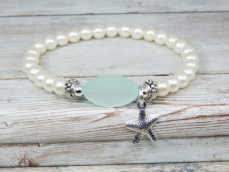 May include: A stretch bracelet featuring white faux pearls, a light blue oval bead, and a silver starfish charm. The bracelet is designed with a beach or nautical theme, perfect for everyday wear or special occasions.