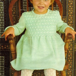 May include: A light green knitted dress with a white lace trim. The dress has a diamond pattern on the bodice and is designed to fit a 22 to 26 inch chest.