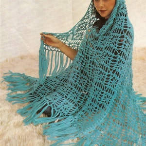 May include: A teal crochet shawl with a fringed edge. The shawl is draped over a person's shoulders and has a delicate, lacy pattern.