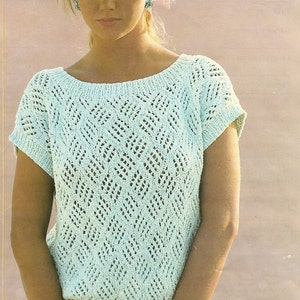 May include: A light blue knitted top with a diamond-shaped openwork pattern. The top has short sleeves and a scoop neck. The model is wearing the top with white shorts.