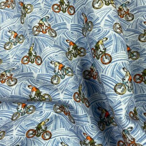 May include: Light blue fabric with a repeating pattern of cyclists on orange bicycles. The cyclists wear orange and green shirts. The background features a white and blue swirling design, creating a textured appearance. This fabric is suitable for apparel or home decor.