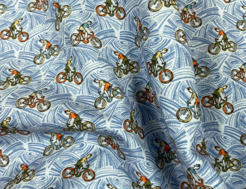 May include: Light blue fabric with a repeating pattern of cyclists on orange bicycles. The cyclists wear orange and green shirts. The background features a white and blue swirling design, creating a textured appearance. This fabric is suitable for apparel or home decor.