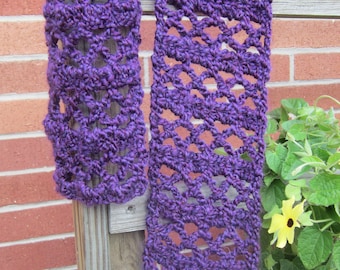 May include: A purple crocheted scarf with a lacy pattern hangs on a wooden fence. The scarf is made with a thick yarn and has a textured look.