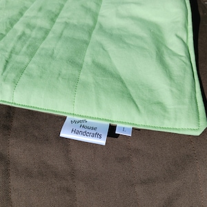 May include: A green quilted cushion with a white label that reads "Myers House Handcrafts" and a white label with the letter "L" on it.