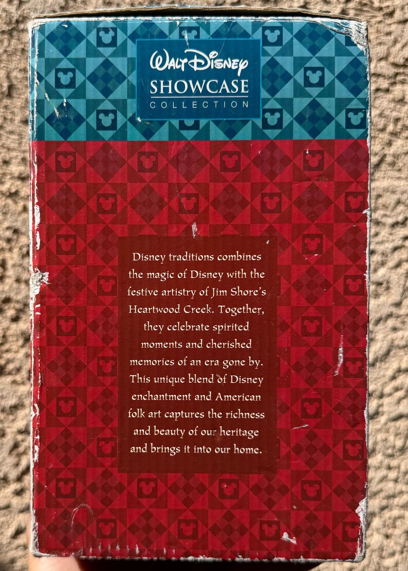 May include: A box featuring the "Walt Disney Showcase Collection" logo. The box has a red and blue geometric pattern with Mickey Mouse icons. Text on the box describes Disney traditions and American folk art.