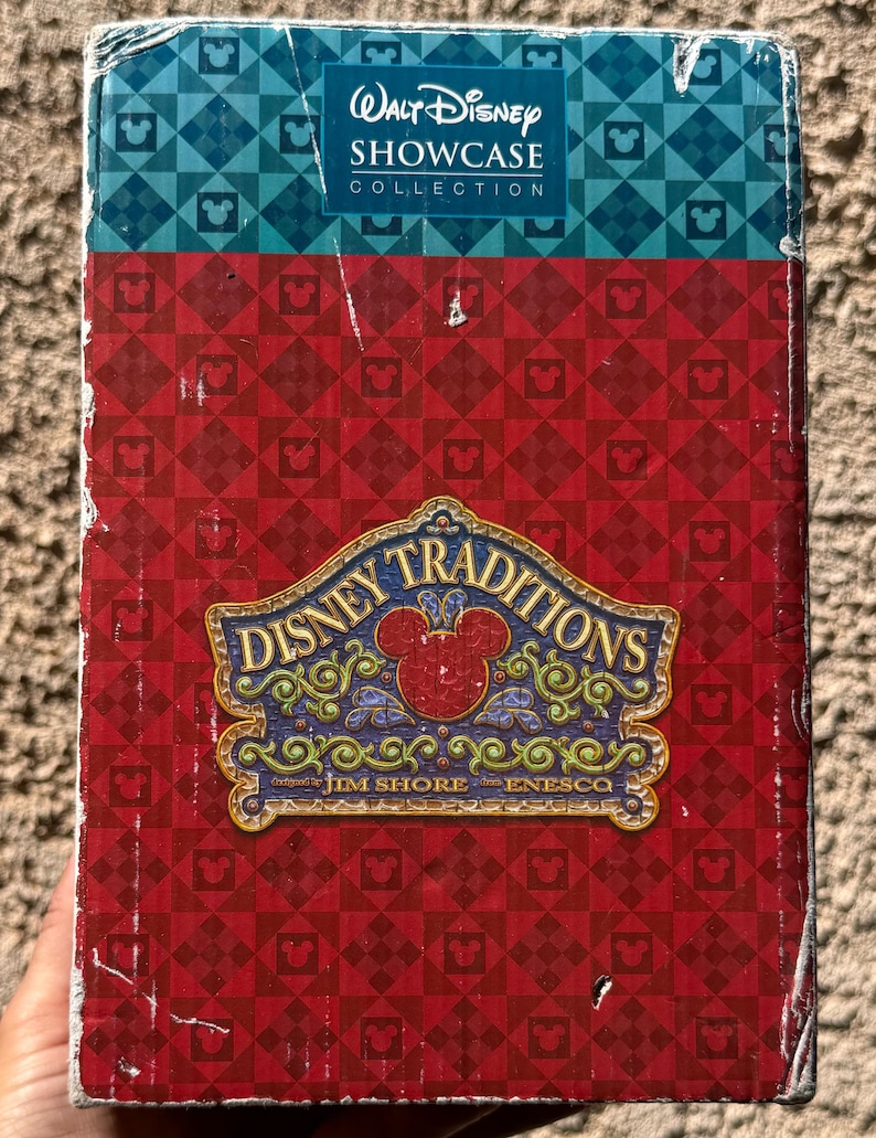 May include: A box with the "Walt Disney Showcase Collection" logo in white on a blue and teal patterned section. The box has a red patterned background with the "Disney Traditions" logo in the centre, featuring a Mickey Mouse head.