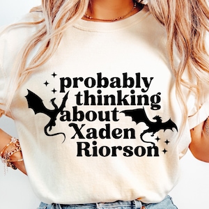 May include: White t-shirt with black text that reads "probably thinking about Xaden Riorson" and two black dragon silhouettes.