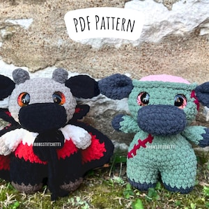 Puede incluir: Dos juguetes de peluche tejidos a crochet, uno vestido de vampiro y el otro de zombie. El vampiro es gris con una nariz negra y una capa roja y blanca. El zombie es verde con un cerebro rosa y puntadas rojas. Ambos juguetes tienen ojos negros y están de pie sobre un fondo de piedra.