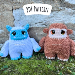 Könnte beinhalten: Zwei gehäkelte Plüschtiere, eines blau und eines braun, mit großen Augen und traurigen Gesichtsausdrücken. Die Spielzeuge sitzen auf einem Bett aus grünem Moos vor einer Steinmauer. Der Text "PDF PATTERN" ist in Schwarz auf einem weißen Oval über den Spielzeugen geschrieben.