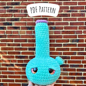 May include: A crocheted plush toy shaped like a bong with a turquoise body, purple rim, and pink eyes. The toy is in front of a brick wall. PDF PATTERN.