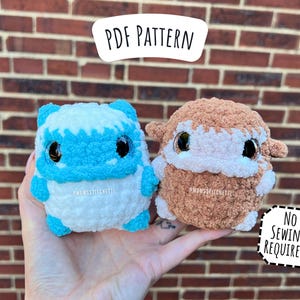 May include: Two plush toys, one blue and white and one brown and white, with big eyes and a fluffy texture. The toys are being held in a hand. The text "PDF PATTERN" is at the top of the image and "NO SEWING REQUIRED!" is at the bottom of the image.