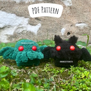 May include: Two crocheted plush toys, one green and one black, with red eyes. The green toy is a Cthulhu-like creature with tentacles and wings. The black toy is a bat with wings. Both toys are sitting on a bed of green grass. The text "PDF PATTERN" is above the toys. The text "@MOMSSITCHETTI" is below each toy.