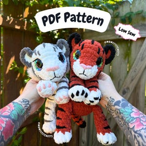 Peut inclure: Deux bébés tigres crochetés, l'un blanc avec des rayures grises et l'autre orange avec des rayures noires, sont présentés. Les bébés ont de grands yeux colorés et des nez roses. L'image comprend le texte "PDF Pattern" et "Low Sew".