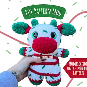 Puede incluir: Modificación de patrón PDF para un juguete de reno de Navidad de crochet. El reno es blanco con rayas rojas y verdes, una nariz roja y cuernos verdes. El texto "MODIFICATION ONLY - NOT FULL PATTERN" está en rojo.