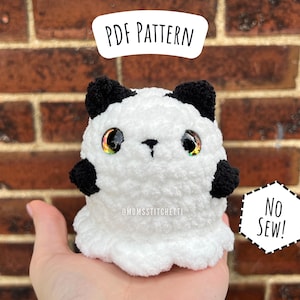 May include: A white and black plush ghost with rainbow eyes. The ghost is sitting on a hand. The text "No Sew!" is on a white sign behind the ghost. The text "PDF Pattern" is on a white sign above the ghost.
