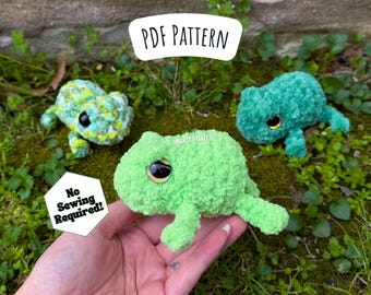 May include: Three crocheted frog plushies in green, light green, and a mottled green and white pattern. The plushies have large, black eyes and are sitting on a bed of green moss. The text "PDF PATTERN" and "No Sewing Required!" are visible in the image.