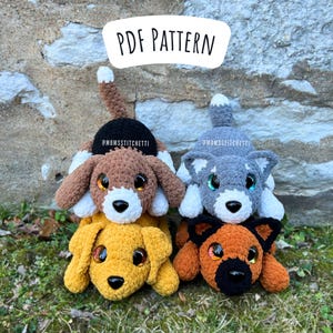 May include: Four crocheted stuffed animals in the shape of dogs. The dogs are stacked on top of each other. The top dog is grey, the second dog is brown, the third dog is yellow, and the bottom dog is orange. The dogs have black eyes and noses. The top dog is wearing a black hat with the text "#MOMSSITCHETTI" on it. The second dog is also wearing a black hat with the text "#MOMSSITCHETTI" on it. The background is a stone wall.