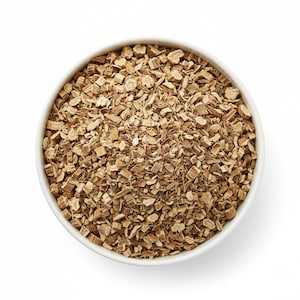 May include: A white round bowl filled with small, irregular, light brown dried root pieces. The contents consist of numerous chopped, woody fragments with a textured, fibrous appearance, evenly distributed within the container against a white background.