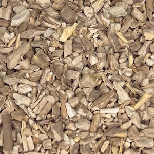 May include: A close-up shot of a collection of chopped wood pieces in shades of brown and beige. The pieces vary in size and shape, with a rough, natural texture. Some pieces resemble small chunks, while others are more like splinters, creating a textured surface.