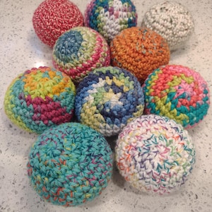 May include: A collection of nine spherical, hand-crocheted balls featuring various yarn colors and textures. The set includes solid red, solid orange, and multi-colored variegated yarn patterns in shades of blue, green, pink, yellow, and white.