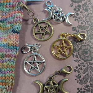 May include: A collection of metal charms with pentagram and crescent moon designs. The charms are in gold, silver, and bronze tones, with lobster clasp attachments. Knitting needles and a colorful knitted piece are also visible.