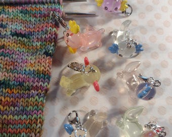 Puede incluir: Una colección de marcadores de punto de axolotl translúcidos y coloridos con cierres plateados. Los marcadores son de varios colores, incluyendo rosa, azul, amarillo y transparente. En la imagen se ve un trozo de tela tejida con un patrón de arcoíris.