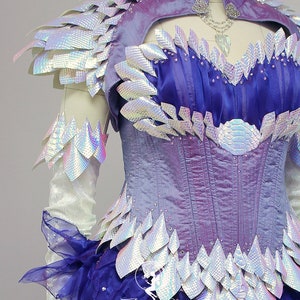 May include: A purple and white corset with iridescent scales and a blue and purple skirt. The corset has a sweetheart neckline and a busk closure. The skirt is made of layers of tulle and has a ruffled hem.